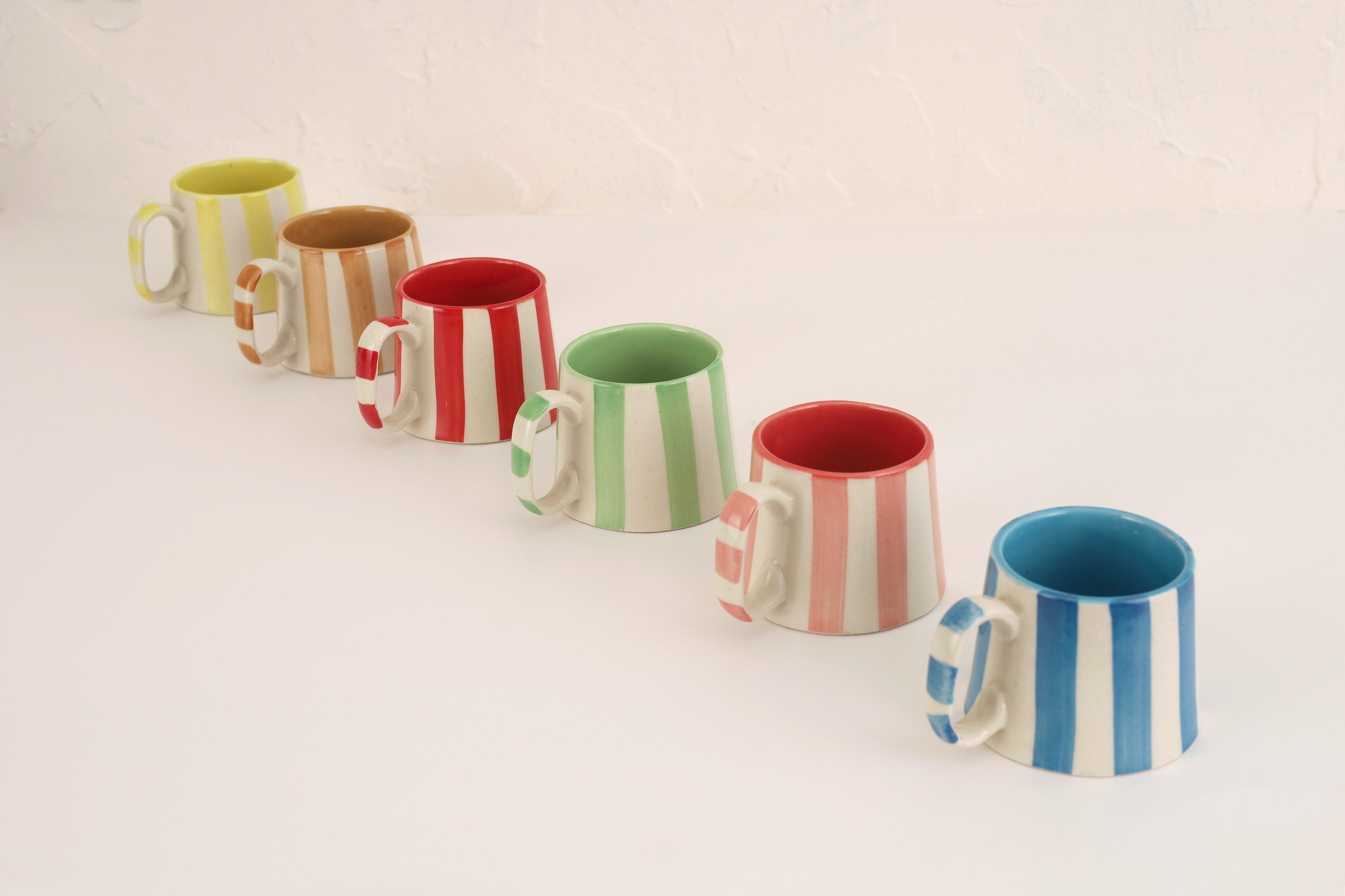 Set of colorful striped ceramic mugs on a light background