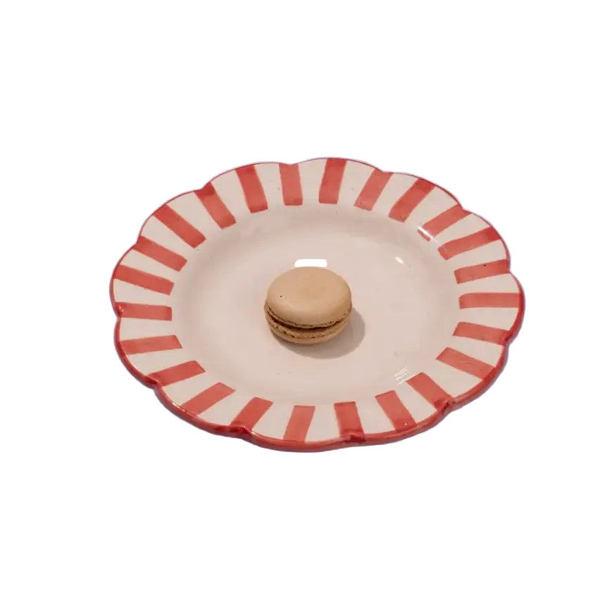 Ceramic plate with red striped rim holding a macaron on a white background
