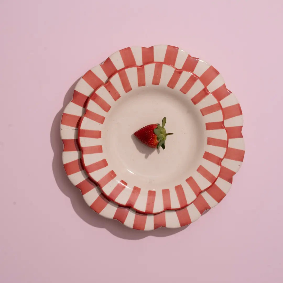 Stack of red and white striped ceramic plates with a strawberry on a pink background