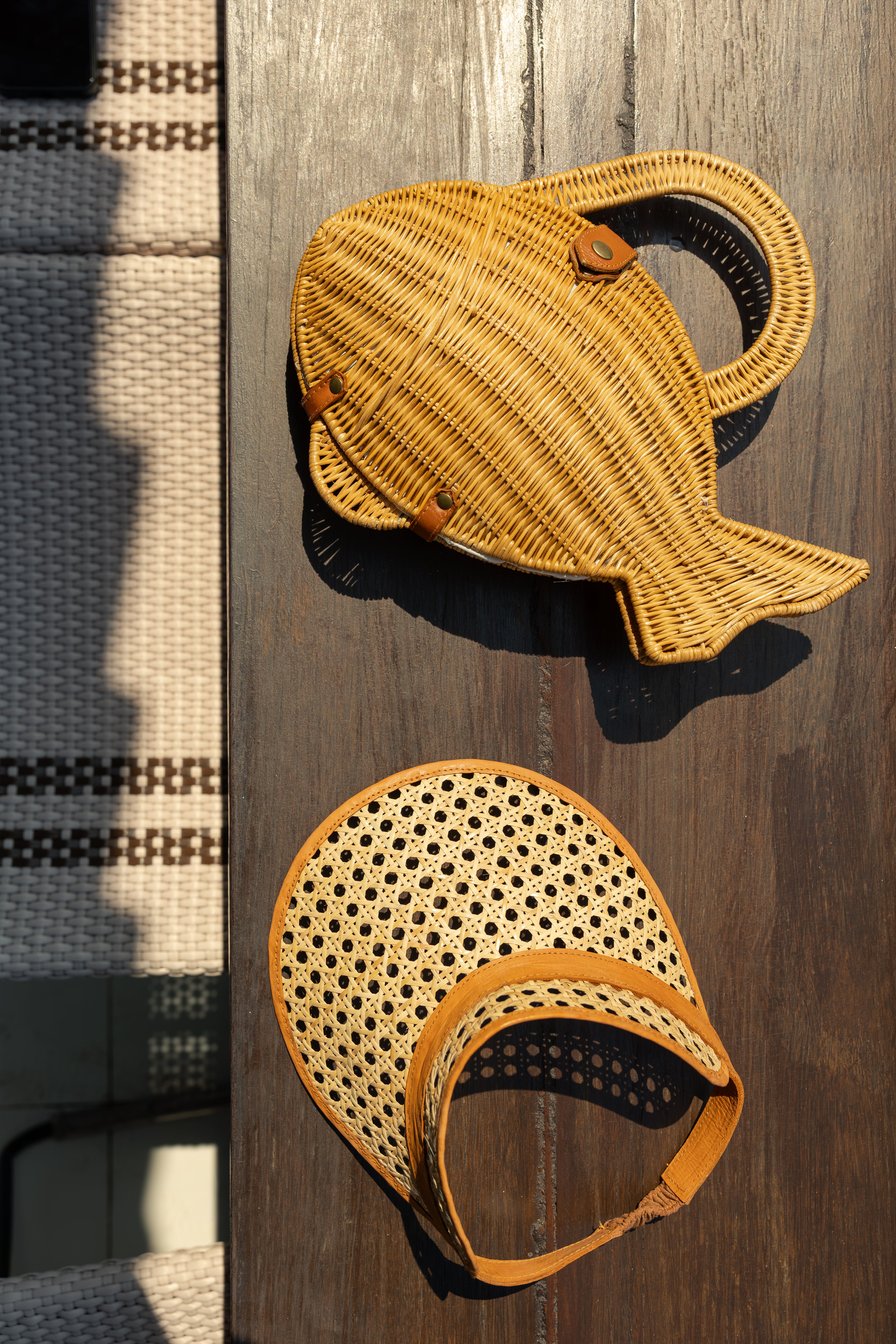 Handwoven rattan fish-shaped basket bag styled next to a cane webbing and leather trim visor hat.