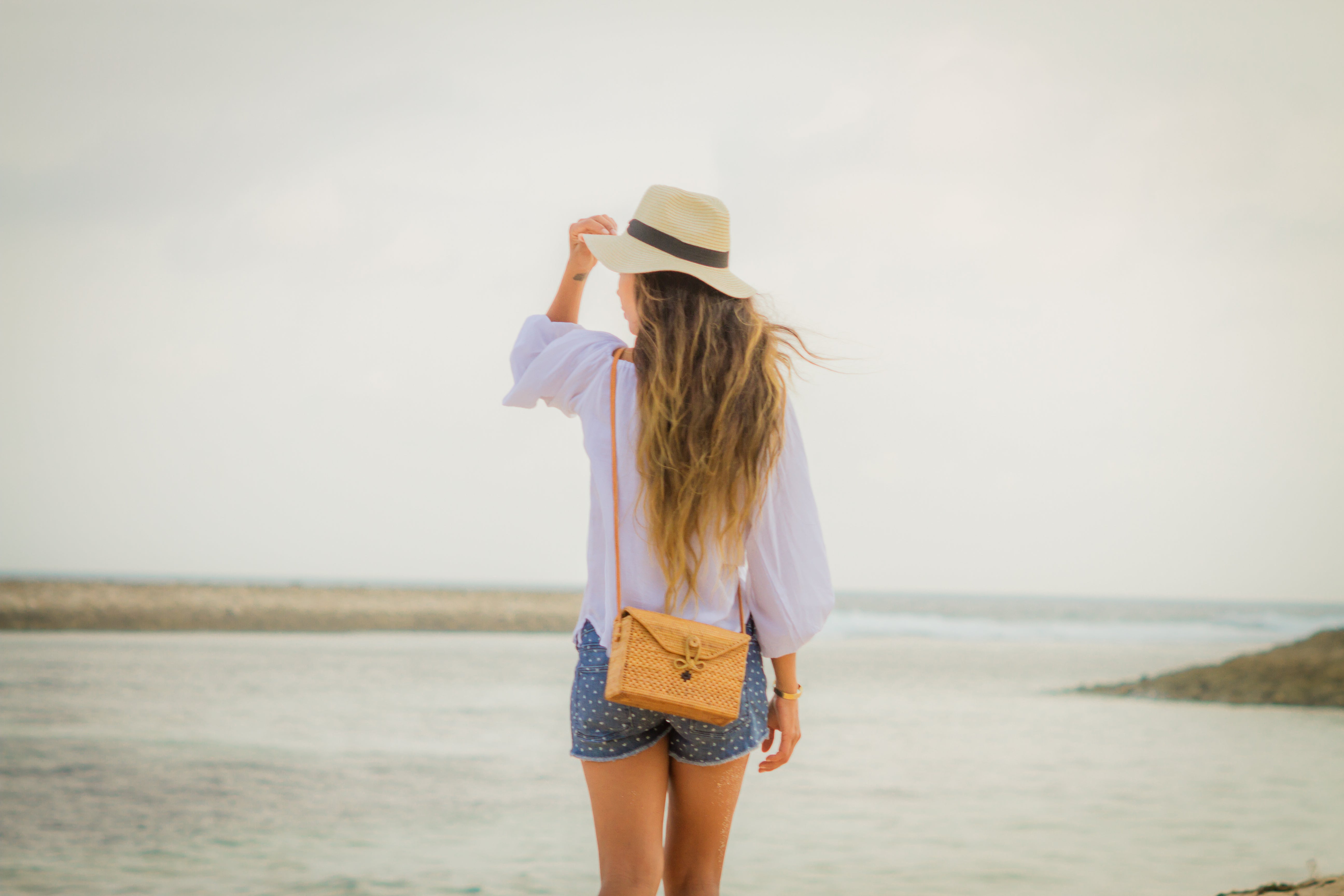 Model on beach wearing bali rattan crossbody bag
