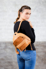 model wearing tan genuine leather mini backpack on one shoulder